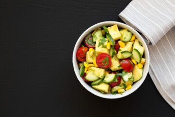 Fresh Avocado Tomato Salad in a bowl on a black background, top view. Flat lay, overhead, from above. Space for text.