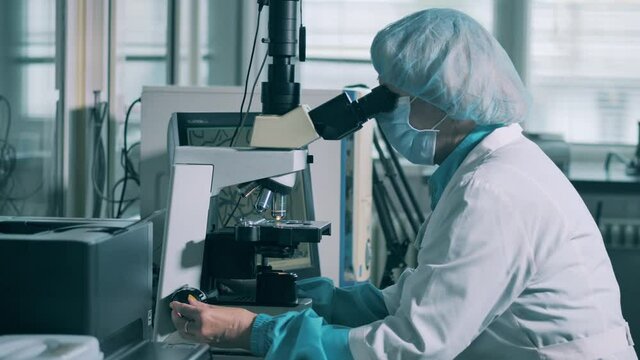 Woman works with microscope in laboratory. Pharmaceuticals production line at a modern pharmaceutical facility.