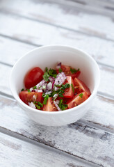 Simple salad with cherry tomatoes, red onion and fresh herbs. Bright wooden background. Close up. 