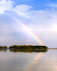 landscape on the river with a rainbow in the blue sky, the edge of the Bank with an autumn forest