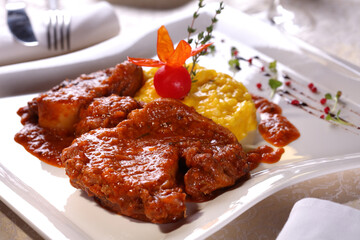 Beef in tomato sauce with yellow risotto and spices on a white plate in a restaurant.