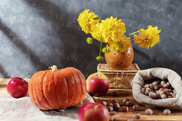 Autumn still life. Apples, hazelnuts, red pumpkin, flowers in a vase, wicker box on a wooden background.