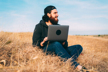 Positive young bearded man working on the computer on a field