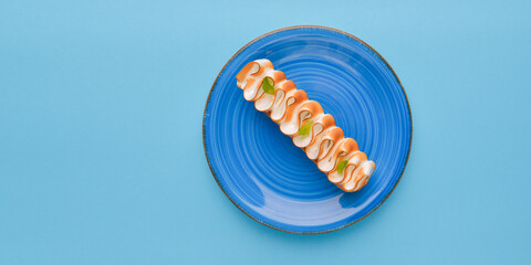 Chocolate eclair with cream on top on plate on pastel blue background. Traditional dessert.