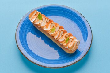 Chocolate eclair with cream on top on plate on pastel blue background. Traditional dessert.