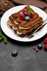 portion of Classic tiramisu dessert with raspberries and blueberries on dark concrete background