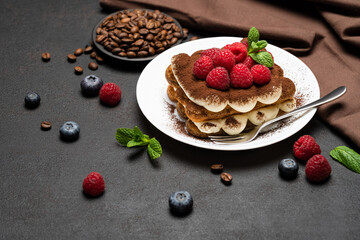 portion of Classic tiramisu dessert with raspberries and blueberries on dark concrete background