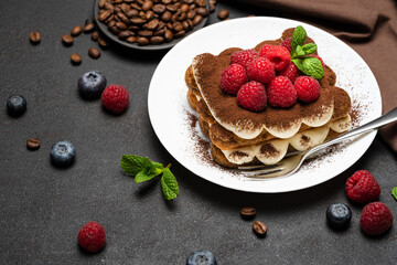 portion of Classic tiramisu dessert with raspberries and blueberries on dark concrete background
