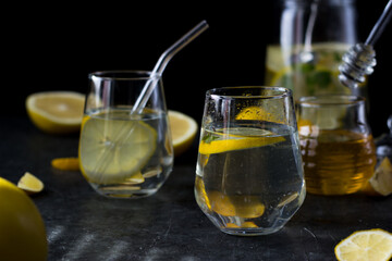 Two glasses of lemonade on a black background. Lemon slices and mint leaves float in the water and lie next to each other on the table