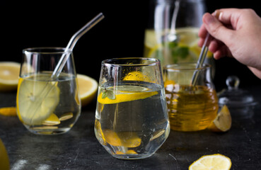 Two glasses of lemonade on a black background. Lemon slices and mint leaves float in the water and lie next to each other on the table