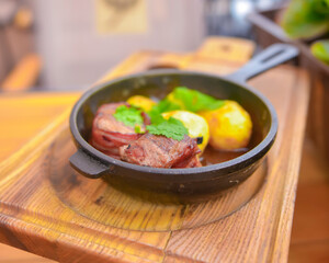 Baked potatoes with grilled bbq steak in a frying pan. Delicious barbecue dinner served on a rustic wooden table.
