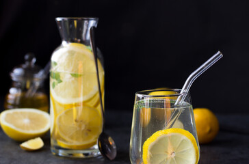 Two glasses of lemonade on a black background. Lemon slices and mint leaves float in the water and lie next to each other on the table