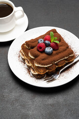 portion of Classic tiramisu dessert with raspberries and blueberries and cup of coffee dark concrete background