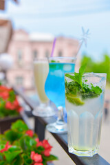 Three fresh juice drinks in tall glasses with plastic straws outside. Milkshake, blue curacao cocktail and mohito.