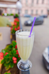 Vanilla milkshake in a tall glass with a plastic straw outside. Delicious dessert drink, refreshing summer beverage.