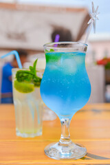 Three fresh juice drinks in tall glasses with plastic straws outside. Milkshake, blue curacao cocktail and mohito.