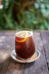 Ice black coffee and lemon in clear glass is placed on the wood table. 