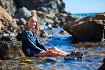 Smiling woman enjoying summer vibe. Meditation and relax concept. Beach vacation. Sharp rocky terrain and virgin nature.
