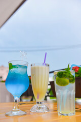 Three fresh juice drinks in tall glasses with plastic straws outside. Milkshake, blue curacao cocktail and mohito.