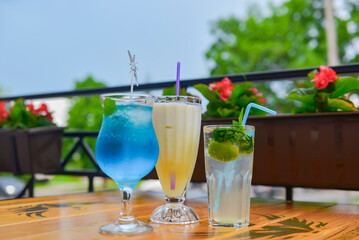 Three fresh juice drinks in tall glasses with plastic straws outside. Milkshake, blue curacao cocktail and mohito.