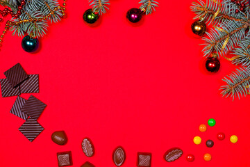 Fototapeta na wymiar Chocolate and candy on a red background with a spruce sprig for Christmas. A banner with a place for text for a pastry shop.