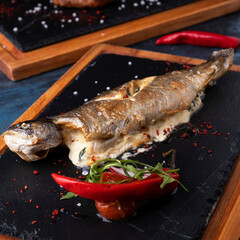 Grilled fish with cheese and pepper on a  black stone. Closeup