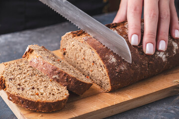 Female hands cutting carrot bread on the wooden board.