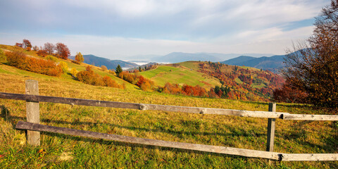 mountainous carpatian rural landscape in autumn. beautiful scenery with wooden fences on grassy rolling hills. trees in fall foliage. clouds on the sky