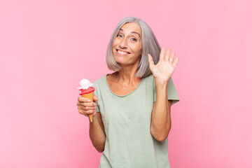 middle age woman smiling happily and cheerfully, waving hand, welcoming and greeting you, or saying goodbye having an ice cream © kues1