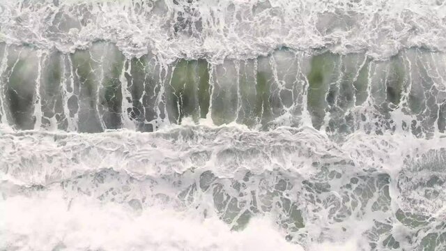 Aerial drone footage of sea waves from ocean to beach, brown sand and emerald water color are contrasted. Beautiful nature footage is 4K 30fps.