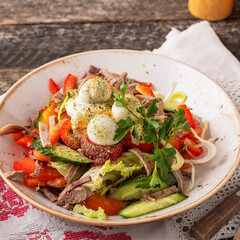 Meat salad with vegetables and quail eggs on wooden rustic background