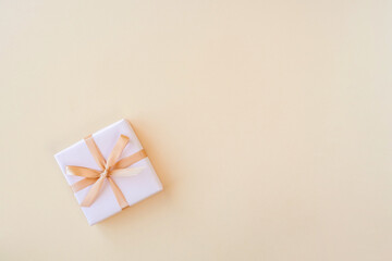 Gift box with gold ribbon and bow on beige background and space for text. Top view