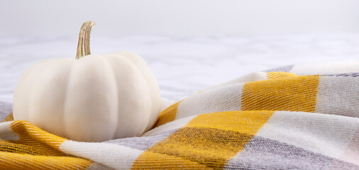 White pumpkin on scarf on marble backdrop. Halloween and thanksgiving day decorations, front view. Copy space