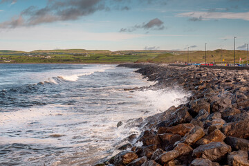 Powerful ocean wave crushes on stone shore. West coast of Ireland, Lahinch town, county Clare. Warm sunny with cloudy sky, Nobody.