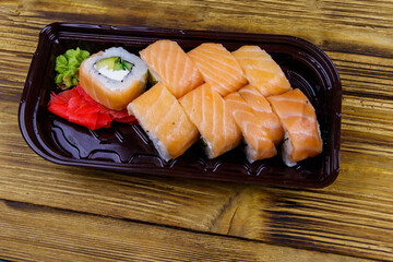 Sushi rolls Philadelphia in plastic box on wooden table. Sushi for take away or delivery of sushi in plastic container