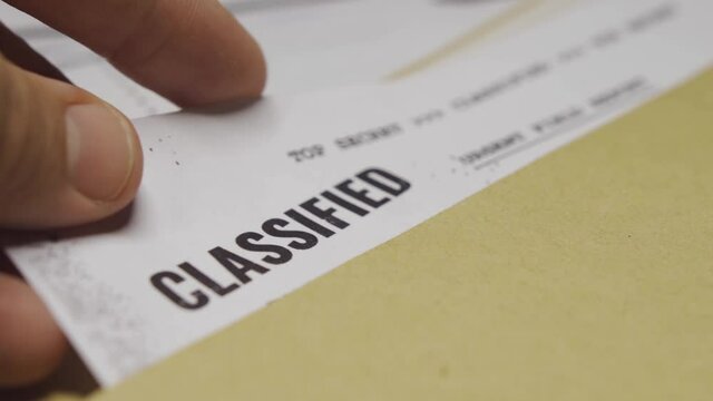 Hand takes out classified document from manila folder. File with top secret info. Government coverup or state secrets. Important leaked papers with sensitive content being put into folder on desk.