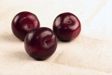 three ripe plum fruit lies on light fabric background