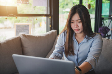 A female Asian office worker of Thai descent is typing and working with notebooks in a coffee shop during the day. She was wearing a blue shirt