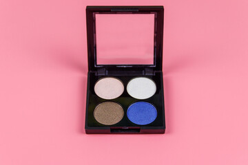 Set of four round eye shadow in a plastic black box on a pastel pink background. Flat lay