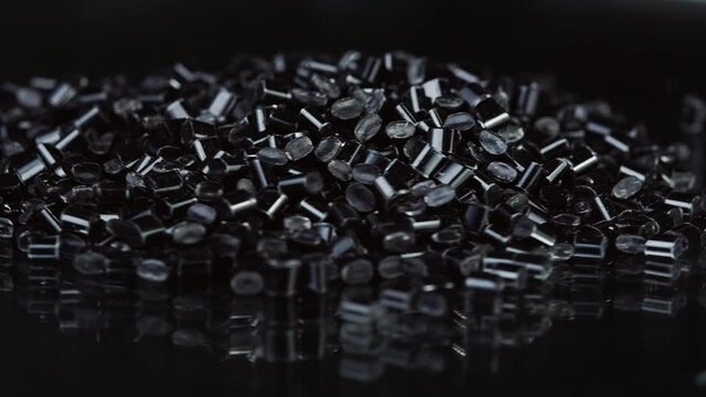 Close-up rotation of black plastic polymer granules on black background