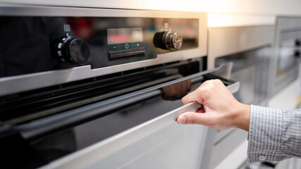 Male hand opening oven door in the kitchen showroom. Buying cooking appliance for domestic kitchen....