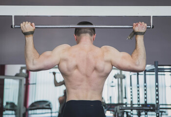 Naklejka premium athlete pulls up in the gym fastening hands on the horizontal bar