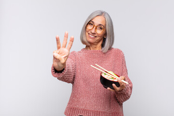 middle age woman smiling and looking friendly, showing number three or third with hand forward,...