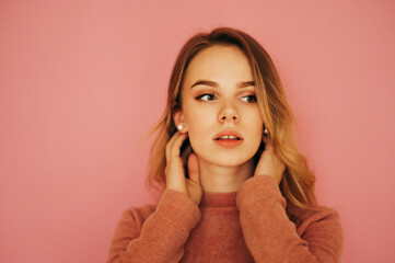 Beauty portrait, lovely young woman isolated on pink background, looking sexy aside, wearing pink sweater.