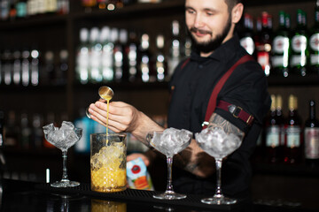 Bartender making refreshing coctail on a bar background. Dark moody style. Ice in the glass. Fosuc on hands