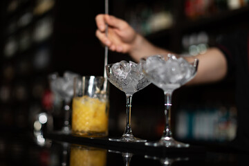 Bartender making refreshing coctail on a bar background. Dark moody style. Ice in the glass. Fosuc on glass