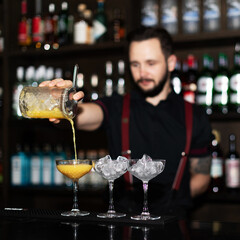 Bartender making refreshing coctail on a bar background. Dark moody style. Ice in the glass. Fosuc on glass
