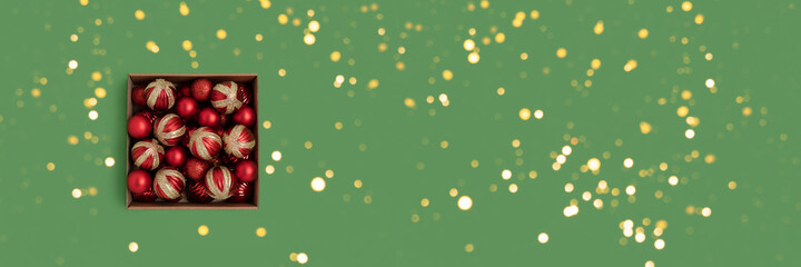 Box with red Christmas baubles on a green background. Festive banner with shiny golden bokeh.