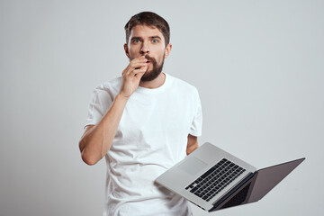 A man with a laptop in his hands on a light background in a white t-shirt emotions light background new technologies