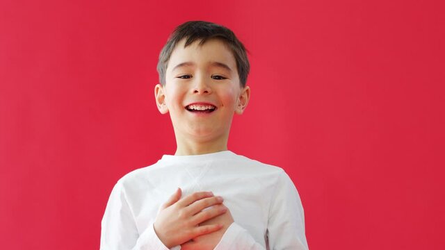 Young casually dressed boy jumps into empty frame from bottom of screen against red studio background smiling and laughing at camera - shot in slow motion